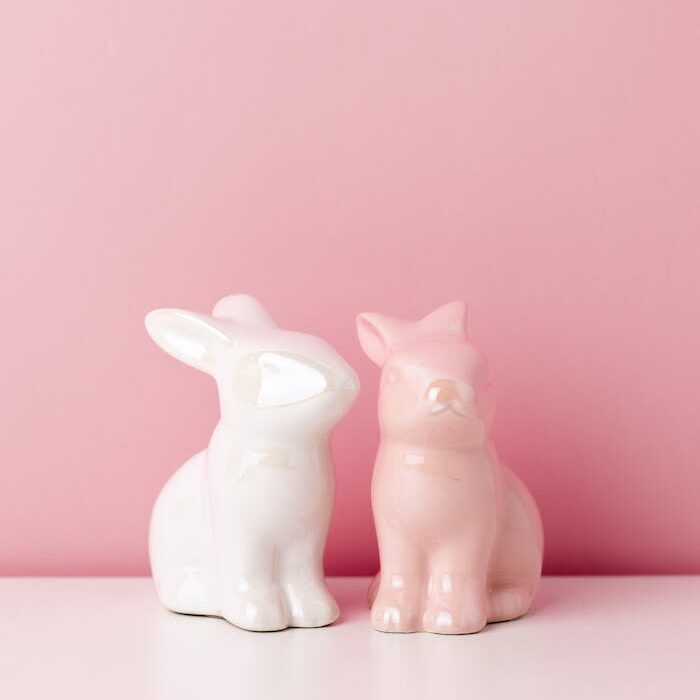 Two pastel ceramic bunny figurines against a pink backdrop, ideal for Easter decor.